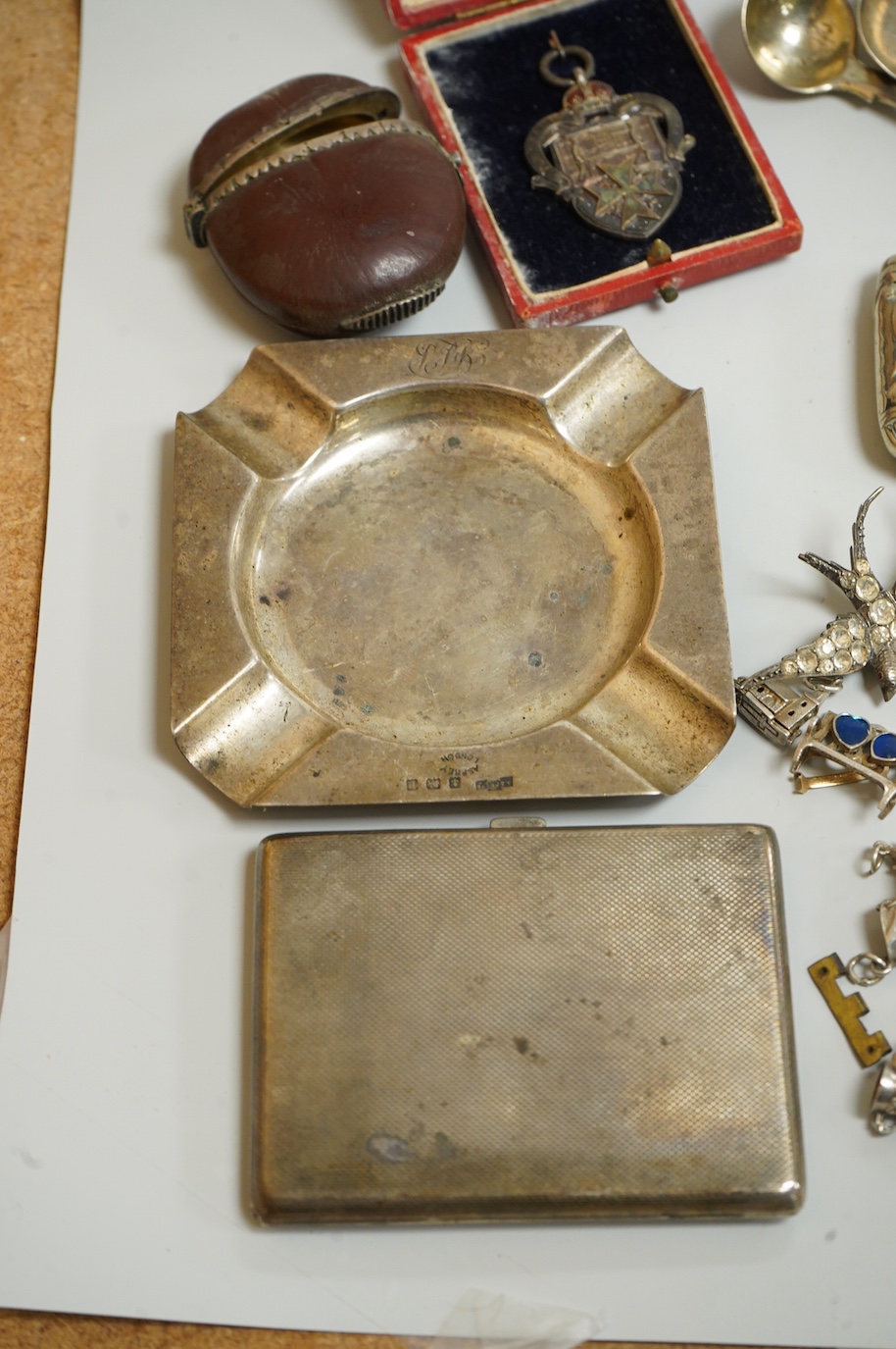 A small collection of silver and white metal charms, including Holy Bible, Penny Farthing, hedgehog and squirrel, together with a silver compact and ashtray, a silver and paste brooch, nut vesta, pipe, etc.